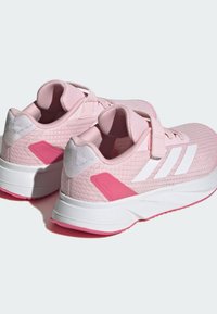 Zapatillas deportivas rosas con una parte superior texturizada, rayas blancas y un acento rosa en el talón. Cuenta con una correa de Velcro para ponerlas y quitarlas fácilmente.