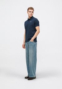 Ναυτικό πόλο μπλουζάκι με κοντά μανίκια, από βαμβακερό ύφασμα. Συνδυάζεται με χαλαρούς, ανοιχτούς μπλε τζιν και σκούρα παπούτσια. Απλός σχεδιασμός, χωρίς ορατά σχέδια.