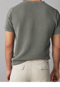 T-shirt a maniche corte, di colore verde oliva, lavorato a maglia con un motivo testurizzato, caratterizzato da un collo rotondo e una vestibilità comoda, abbinato a pantaloni beige chiaro.