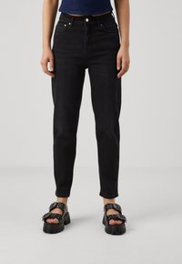 Svart hög midja jeans med rak passform, med framfickor och bälteshällor. Kombinerat med tjocka svarta sandaler med spännen.