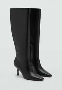 Botas de cuero negras hasta la rodilla con punta afilada, tacón ligero, diseño minimalista y detalle de cremallera lateral. Textura suave.