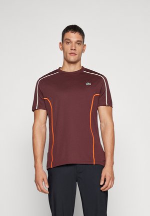 Maglietta atletica bordeaux con piping arancioni sui lati e dettagli bianchi. Presenta un collo tondo e un logo verde sul lato sinistro del petto.
