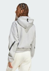 Γκρίζα φούτερ με εφαρμοστό μέρος στη μέση, φαρδιές μανίκες, μαύρες λωρίδες στα μανίκια και μεγάλο καπέλο. Το υλικό φαίνεται μαλακό και με υφή.