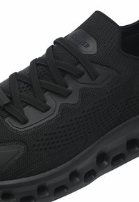 Černá atletická bota s pleteným svrškem, texturovanými akcenty a polstrovanou podešví s kruhovými otvory pro prodyšnost.