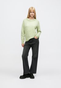 Lichtgroene trui met een ronde hals en lange mouwen, gecombineerd met hoge taille donkergrijze wijde pijpen jeans en zwarte plateau laarzen.