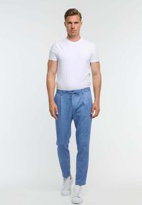 Pantalones ajustados de color azul claro, confeccionados en tejido tejido, con cintura ajustable, corte entallado y bolsillos laterales, combinados con una camiseta blanca lisa y zapatillas blancas.