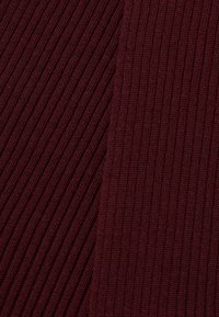 Kamera u krupnom planu prikazuje rebrastu burgundsku pleteninu s dijagonalnim i vertikalnim rebrastim uzorcima i teksturom.