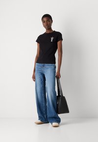 Black cotton t-shirt with short sleeves and a star emblem, paired with loose blue jeans and a black bag. Light-colored shoes.