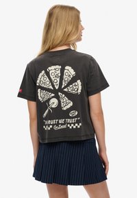 Camiseta negra con un gráfico de pizza que incluye porciones, un cortador de pizza y el texto "EN EL ÓXIDO CONFIAMOS" en blanco. Corte informal con mangas cortas.