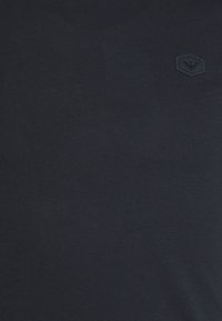 Mörkblått tyg med en liten svart hexagonal lapp som har en präglad örnlogotyp på den övre högra sidan.