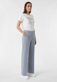 Biała koszulka z nadrukiem "WILD WILD WEST" w kolorze czarnym, połączona z jasnoniebieskimi szerokimi spodniami i białymi trampkami.