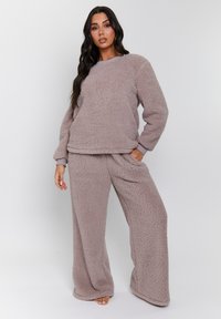 Conjunto de loungewear de felpa en un suave tono malva, que incluye una sudadera de manga larga y pantalones de pierna ancha con bolsillos, textura suave y ajuste relajado.
