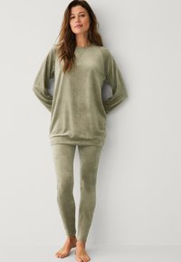 Olive zelený lounge set vyrobený z měkké, sametové látky; obsahuje volně střiženou dlouhou halenku a těsně přiléhající legíny, oboje s minimem švů.