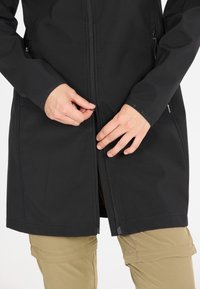 Svart softshell-jacka med dragkedja fram, ståkrage och två sidofickor. Har en jämn, matt yta.