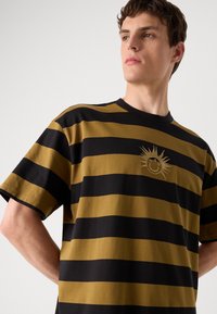 Gestreepte t-shirt in zwart en goud, met korte mouwen, ronde hals en een geborduurde zonafbeelding op de borst. Katoenmateriaal.