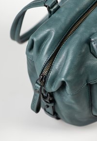 Teal leren tas met een zachte textuur, voorzien van een ritssluiting, verstelbare schouderband en een geplooid ontwerp met subtiele stiksels.