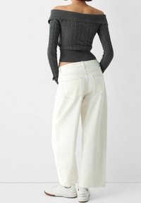 Gray off-the-shoulder knit sweater with a textured pattern paired with loose white wide-leg jeans and white sneakers, showing back view.