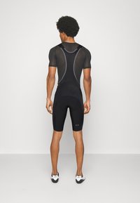 Combinaison de vélo noire avec un haut à manches courtes et un bas jusqu'aux genoux. Fabriquée en tissu texturé et respirant, dotée de panneaux en maille et d'un logo.