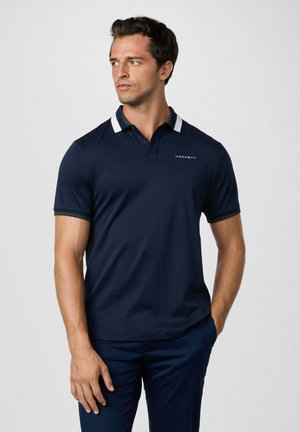 Camisa polo de marina de manga corta, con cuello a rayas blancas y verdes, logo bordado "HACKETT" en el pecho. Textura suave y diseño ajustado.
