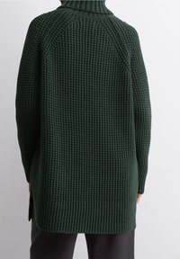 Langer, dunkelgrüner, grob gestrickter Pullover mit hohem Kragen, gerippten Ärmelbündchen und seitlichen Schlitzen für eine lockere Passform. Strukturiertes, oversized Design.