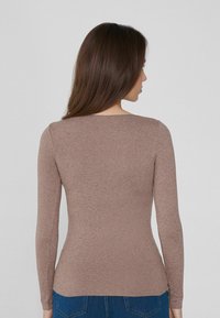 Top ajustado de manga larga en tejido marrón claro con una textura suave y un escote redondeado, combinado con jeans de mezclilla azul.