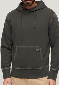 Dark grey hoodie made of soft fabric, featuring a kangaroo pocket, drawstring hood, and contrasting stitching with a small brand tag.