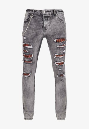 Šedé opotrebované džínsy s viacerými roztrhnutiami, ktoré odhaľujú červenú a čiernu kockovanú látku pod nimi. Má bočný detail reťaze a zúžený strih.