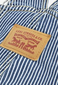 Tissu en denim bleu à rayures avec des coutures jaunes, présentant une patch en cuir tan embossé avec "Levi Strauss & Co." et un graphique de cowboy.