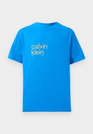 Spoža spilgtā zila kokvilnas T-krekla ar īsām piedurknēm, kuram priekšpusē ir liela dzeltena "calvin klein" logo un teksts "new york city / since 1981".
