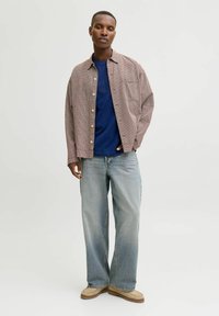 Camisa de cuadros rojos y blancos sobre una camiseta de cuello redondo azul, combinada con jeans de pierna ancha de color azul claro y zapatos sin cordones de color beige.