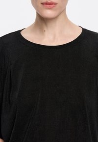 Maglia nera con scollo rotondo, caratterizzata da una leggera lucentezza e una vestibilità rilassata, che mette in risalto la morbidezza del tessuto e un design semplice.