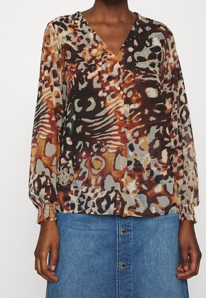 Brun og beige mønstret bluse med V-hals, lange ærmer og knaplukning. Stoffet er gennemsigtigt med samlede manchetter, parret med en denimnederdel.