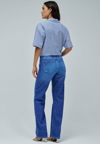 Camicia a maniche corte a righe blu chiaro abbinata a jeans blu a vita alta. I jeans presentano un classico design a cinque tasche e gamba dritta.