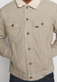 Beige kordjacka med fårskinnskrage, framknäppning, två bröstfickor och en något figursydd design. Texturerad tyg, avslappnad stil.
