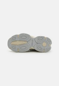 Semelle de sneaker en gris clair et beige, avec des motifs texturés pour l'adhérence, portant le mot "REPLAY" en relief sur le côté.