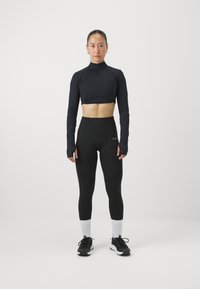 Svart, kortermet langermet topp med glidelås i halsen, kombinert med høyt liv svarte leggings. Match med svarte treningssko og hvite ankelsokker.
