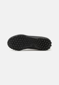 Suela de zapato deportivo negro con un patrón de tracción hexagonal y circular, logo de Adidas visible cerca del arco en un fondo blanco.