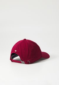 Cappellino da baseball cremisi con visiera curva, texture in tessuto, cinturino posteriore regolabile e un piccolo dettaglio in bianco con la scritta "85".