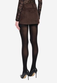 Brązowa zamszowa spódnica z dopasowaną talią, czarne nieprzezroczyste rajstopy i czarne szpilki; charakteryzuje się równym dołem i gładką fakturą.