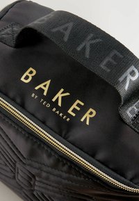 Borsa nera trapuntata con una cerniera dorata. Presenta il testo "BAKER by TED BAKER" in oro. Include una maniglia in tessuto nero con il marchio.