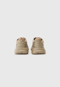 Beige sneakers with a textured fabric upper, rounded toe, cushioned sole, and "HUGO" branding on the back heel.