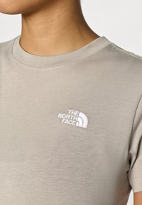 Μπεζ βαμβακερό T-shirt με στρογγυλή λαιμόκοψη, με λευκό κεντημένο λογότυπο "The North Face" στο αριστερό στήθος. Κοντά μανίκια.