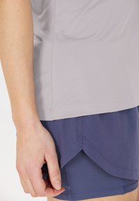 Handen vilar bredvid lager av träningskläder: en ljusgrå topp över marinblå shorts och kjol med en scallopkant.