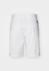 Hvite bomullsshorts med rett snitt, oppbrettede kanter og to baklommer. Har et lite logo-merke på høyre baklomme.