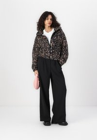 Faux fur cropped jacket in black and pink leopard print, paired with black wide-leg trousers and a small pink handbag.