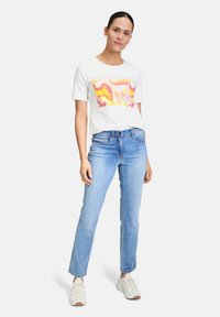 White cotton t-shirt with colorful abstract design, paired with light blue denim jeans. White sneakers complete the outfit.