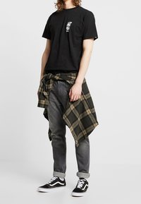 Musta puuvillainen t-paita, jossa pieni kalloaiheinen kuva, yhdistetty harmaisiin farkkuihin ja mustavalkoisiin lenkkareihin. Vyötäröllä ruudullinen flanellipaita solmittuna.