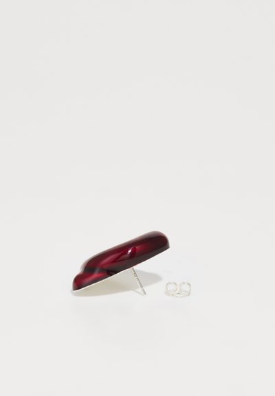 Κόκκινη και μαύρη μαρμάρινη τσιμπίδα μαλλιών με γυαλιστερή φινίρισμα, διαθέτοντας ασημένια μεταλλική λεπτομέρεια και μια διαφανή ελαστική ταινία κοντά.