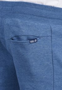 Pantalons de survêtement bleus en tissu texturé, avec une petite poche au dos et une étiquette indiquant « ISOLID ». Taille élastique pour le confort.