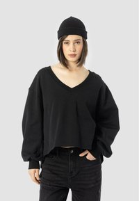 Black cropped sweatshirt with a deep V-neck, oversized sleeves, and ribbed cuffs, paired with black high-waisted jeans.